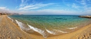 Panoramic Red Sea shoreline in Egypt with clear turquoise water, a pebbled beach, and mountains in the distance