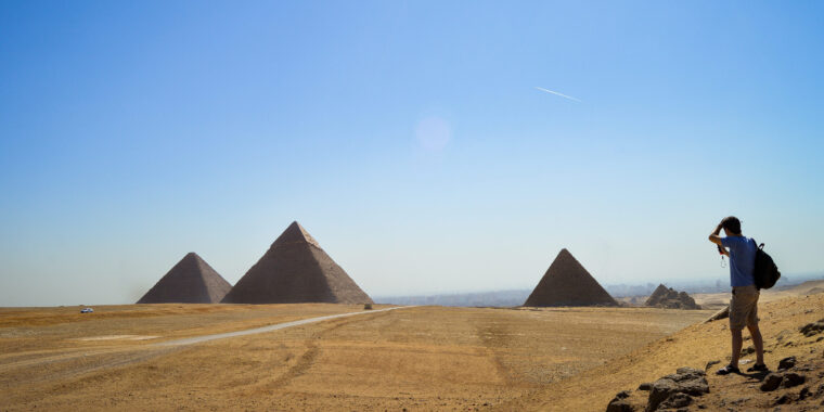 Visitor standing on the Giza Plateau overlooking the pyramids of Khufu, Khafre and Menkaure with smaller subsidiary pyramids visible across the desert