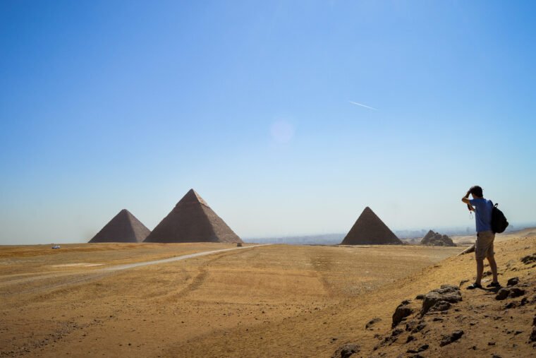 Visitor Overlooking the Pyramids of Khufu, Khafre and Menkaure at Giza Visitor standing on the Giza Plateau overlooking the pyramids of Khufu, Khafre and Menkaure with smaller subsidiary pyramids visible across the desert