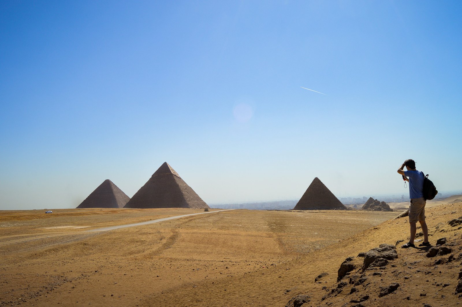 Visitor standing on the Giza Plateau overlooking the pyramids of Khufu, Khafre and Menkaure with smaller subsidiary pyramids visible across the desert
