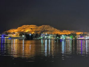 Illuminated rocky hillside and buildings reflected in dark Nile water at night