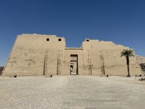 Sandstone entrance pylon at Medinet Habu in Luxor with carved hieroglyphs and a palm tree