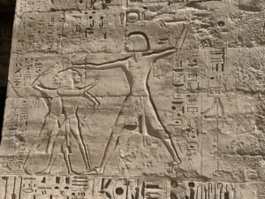 Ancient Egyptian relief of a pharaoh striking a captive beside hieroglyphic inscriptions at Medinet Habu