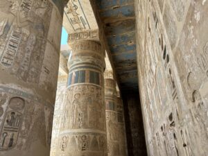 Columned passage at Medinet Habu with Ramesses III cartouches, ritual reliefs and surviving blue, green, red and yellow pigment across column bands and ceiling