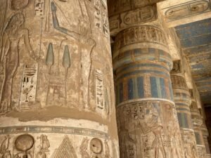 Ancient Egyptian temple columns with carved figures, hieroglyphs, and preserved blue paint at Medinet Habu