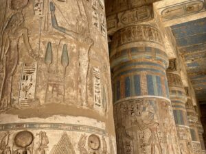 Close view of Medinet Habu columns with Ramesses III cartouches, ritual scenes and preserved blue, green and red painted bands beneath a blue-painted ceiling