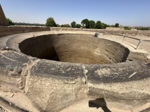 Circular stone opening of the ancient nilometer at the Temple of Kom Ombo with Nile-side greenery beyond