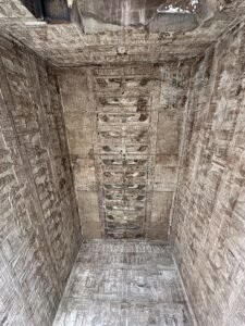 Narrow ancient Egyptian temple chamber with hieroglyphs and carved reliefs covering the ceiling and walls