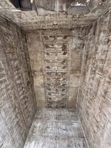 Upward view inside the Temple of Hathor at Dendera showing a richly carved astronomical ceiling with winged solar emblems, star fields and surrounding hieroglyphic ritual reliefs
