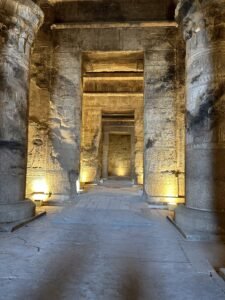 Long stone corridor lined with carved columns and hieroglyphic doorways inside Dendera Temple in Egypt
