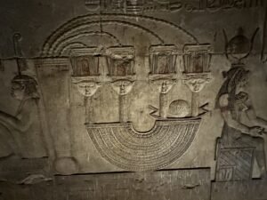 Carved relief at Dendera showing Hathor-faced ritual emblems framed by Egyptian deities and hieroglyphs