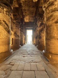 Warmly lit stone passage between carved columns inside the Temple of Hathor at Dendera, Egypt
