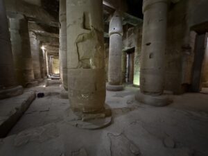 Dim interior of Seti I’s temple at Abydos with rows of papyrus-bud columns carved with standing royal and divine figures, ritual scenes and hieroglyphic bands
