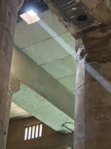 Beam of sunlight entering through a roof opening between ancient stone columns at the Temple of Seti I in Abydos, Egypt