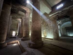 Dim column hall at the Temple of Seti I in Abydos, Egypt, with sunlight streaming through roof openings