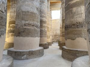 Rows of massive sandstone columns with carved figures and hieroglyphs in Karnak Temple’s Great Hypostyle Hall