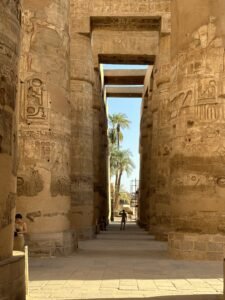 Hieroglyph-covered columns framing a sunlit passage and palm trees inside Karnak Temple