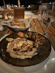 Grilled chicken with roasted vegetables, lime, bread, and a water glass at an outdoor restaurant in Luxor