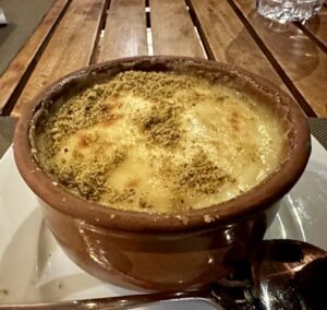 Warm Egyptian Umm Ali dessert baked in a clay pot with a creamy golden topping and crushed nuts