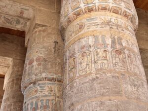 Massive papyriform columns in Karnak’s Great Hypostyle Hall covered with painted Ramesside royal cartouches, ritual scenes and hieroglyphic bands in red, blue, green and yellow