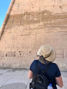 Visitor studying large Ptolemaic relief scenes and hieroglyphic inscriptions on a wall of the Temple of Horus at Edfu in Upper Egypt