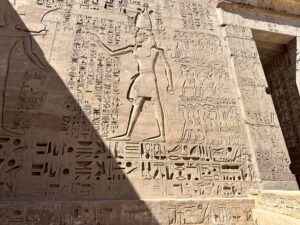 Monumental Ptolemaic relief at Edfu Temple showing the king striding beside several registers of bound or subdued foreign captives with dense hieroglyphic inscriptions