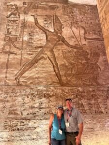 Monumental relief of Ramesses II striking enemies at Abu Simbel with visitors standing beneath the carved scene