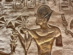 Relief inside the Great Temple at Abu Simbel showing Pharaoh Ramesses II carrying stylized ritual floral bouquets beneath his royal cartouches and surrounding hieroglyphs