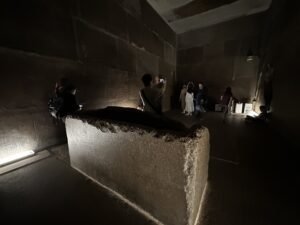 Open granite sarcophagus inside the King’s Chamber of the Great Pyramid of Khufu with visitors nearby