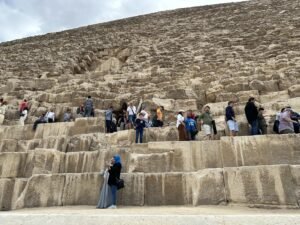 Visitors standing on massive limestone courses below the entrance of the Great Pyramid of Khufu on the Giza Plateau