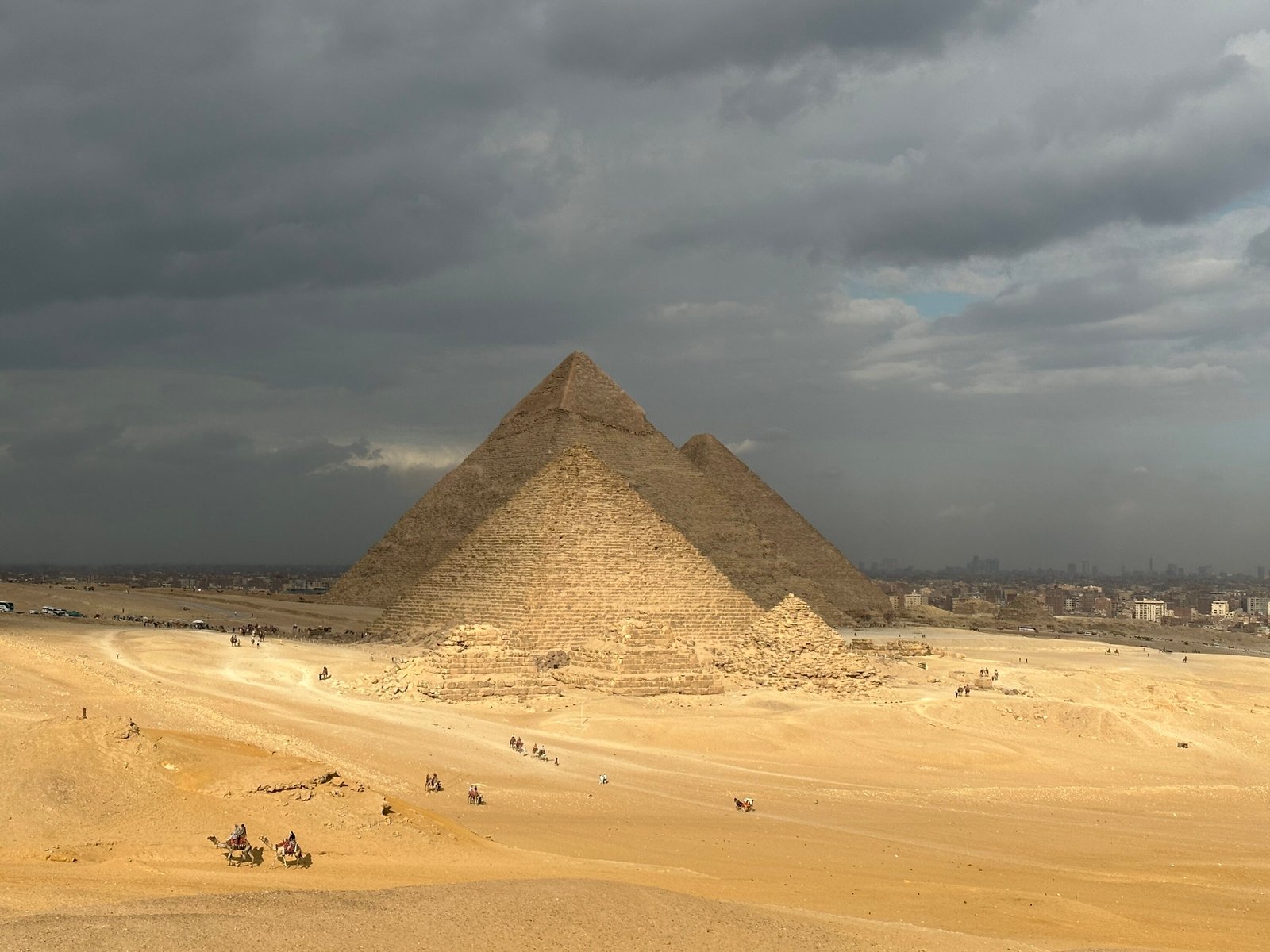 Pyramids of Menkaure, Khafre and Khufu aligned across the Giza Plateau beneath dramatic clouds