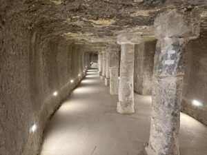 Long rock-cut underground corridor lined with stone columns and floor lights at Saqqara