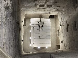 View down into an ancient rock-cut burial chamber with a stone structure at Saqqara