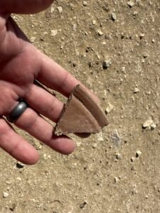 Small reddish-brown pottery sherd held in a hand at the Saqqara archaeological site
