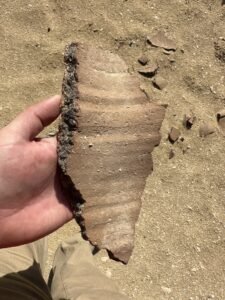 Large reddish-brown pottery sherd with horizontal ridges held in a hand at Saqqara