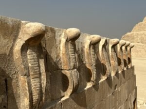 Row of carved cobra uraei along a stone wall in Djoser’s Step Pyramid complex at Saqqara