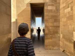 Visitors walking through a narrow stone entrance passage in Djoser’s Step Pyramid complex at Saqqara