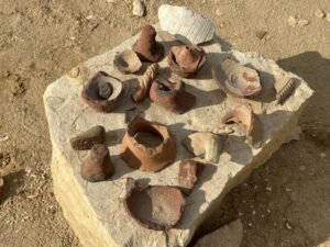 Collection of reddish-brown ancient pottery sherds arranged on a pale stone block at the Hawara archaeological site in Egypt