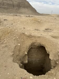 Rectangular open archaeological shaft in the desert at Hawara with the Pyramid of Amenemhat III rising behind it