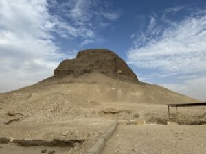Heavily eroded mudbrick Pyramid of Senusret II at Lahun rising from a sandy desert mound beneath a blue and cloudy sky