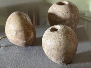 Three rounded stone objects, two with drilled holes, displayed together in an Egyptian museum case