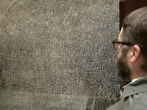 Visitor studying a large dark stone slab densely covered with rows of Egyptian hieroglyphs in a museum