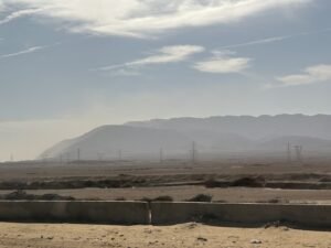 Low desert mountain range beyond a flat arid plain crossed by electrical transmission towers in Egypt