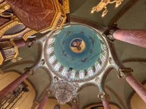 Painted church dome with stained-glass windows, marble columns, and a hanging chandelier in Coptic Cairo