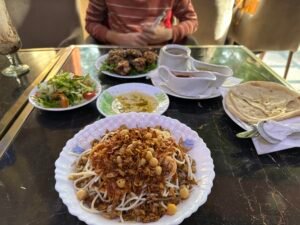 Plate of Egyptian koshari with chickpeas, fried onions, rice, pasta, and lentils served with bread and side dishes