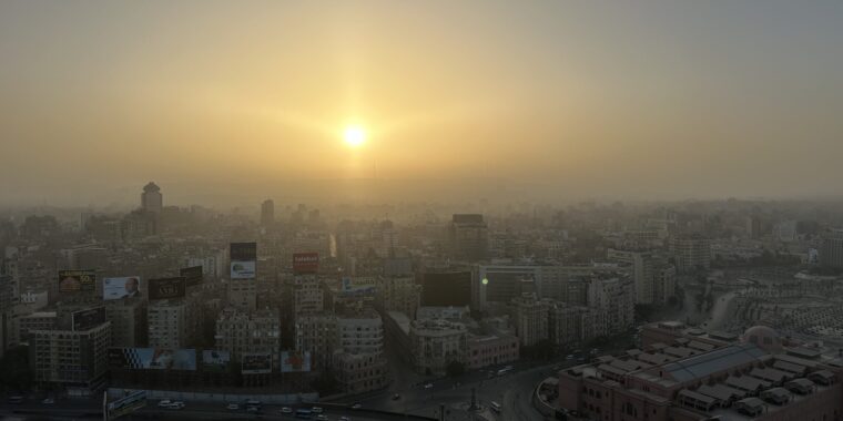 Golden sunrise above Cairo’s hazy city skyline with roads and buildings in the foreground