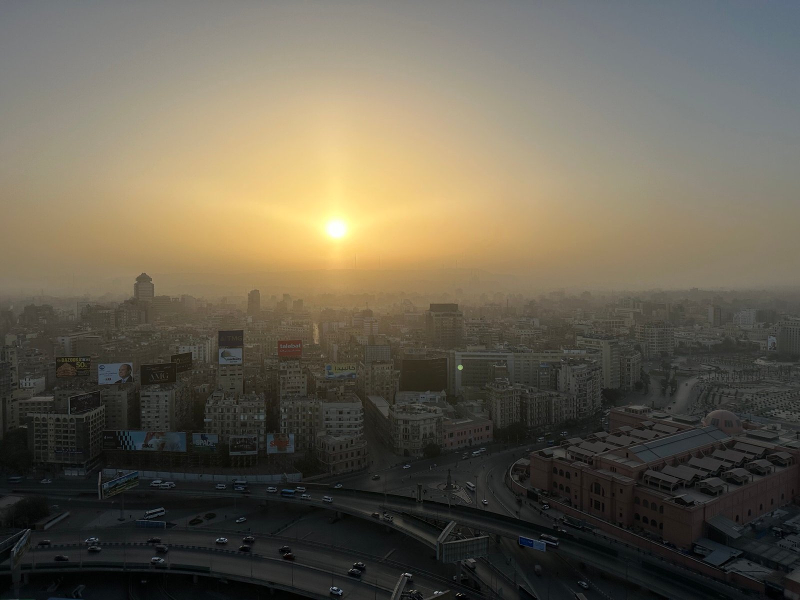 Golden sunrise above Cairo’s hazy city skyline with roads and buildings in the foreground
