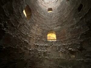 Looking upward inside a tall circular pigeon tower with rough brick walls and small nesting openings
