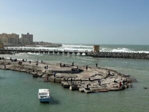 Stone breakwater and small boat on the Mediterranean coast beside the Citadel of Qaitbay in Alexandria, Egypt