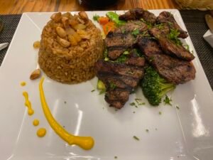 Plate of grilled meat with seasoned rice, broccoli, carrots, and sauce at an Egyptian restaurant